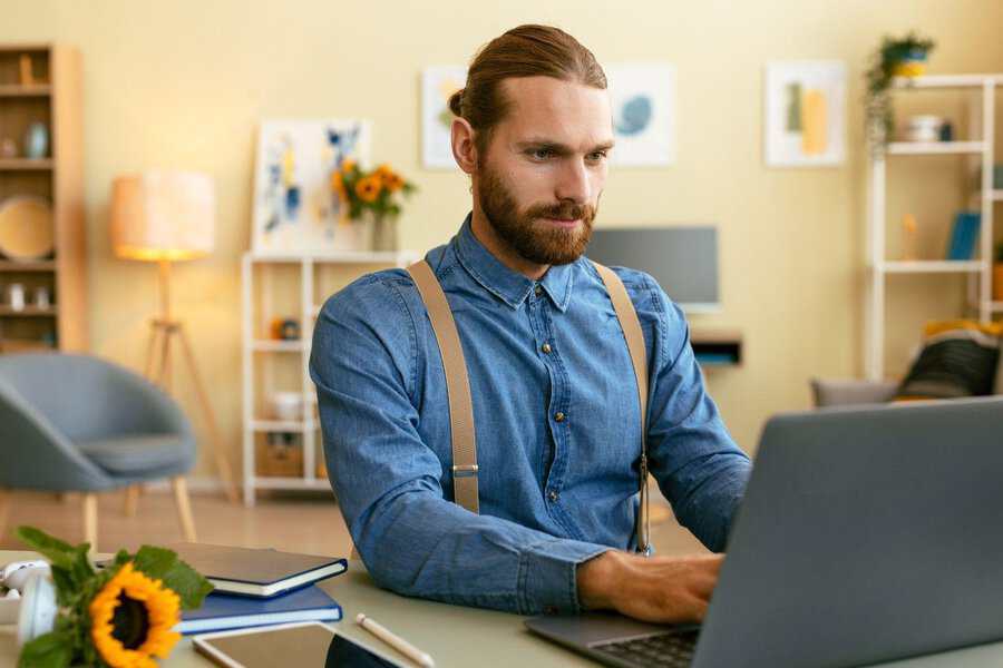 Man with a beard works on his laptop in a cozy home office, checking Ukrainiancharm reviews for safety and legitimacy