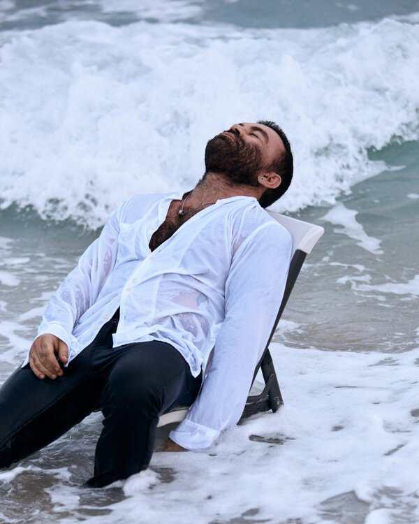 Man in wet white shirt leans back on a chair in ocean waves during Miami photoshoot, eyes closed and looking relaxed