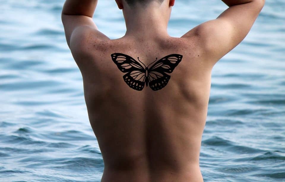 large black and grey tattoo on man's upper back of a bold realistic butterfly