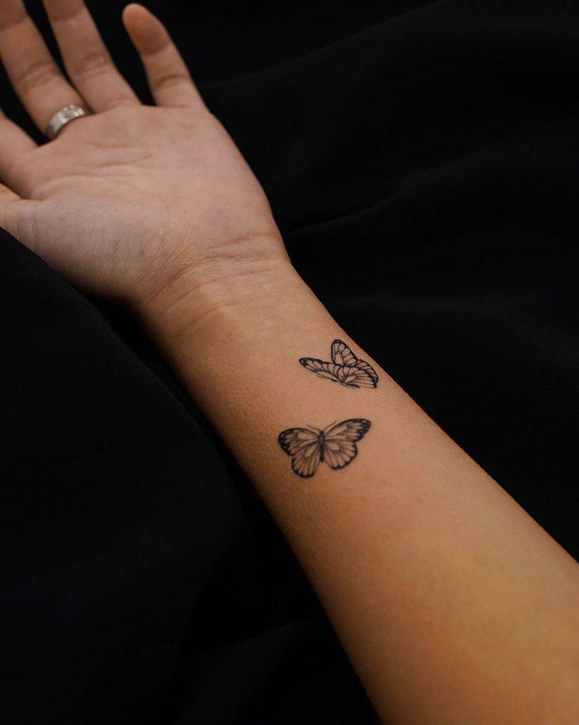 tiny black and grey tattoo on woman's inner forearm of two realistic butterflies
