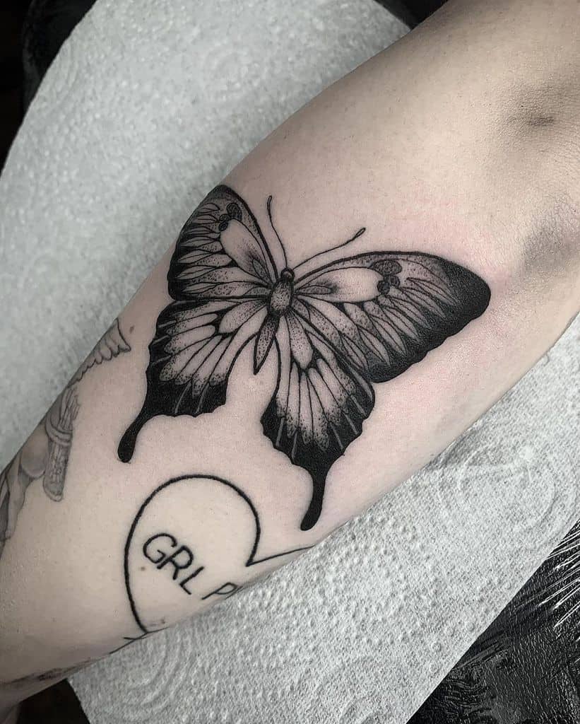 medium-sized black and grey tattoo on woman's lower leg of a dark realistic butterfly
