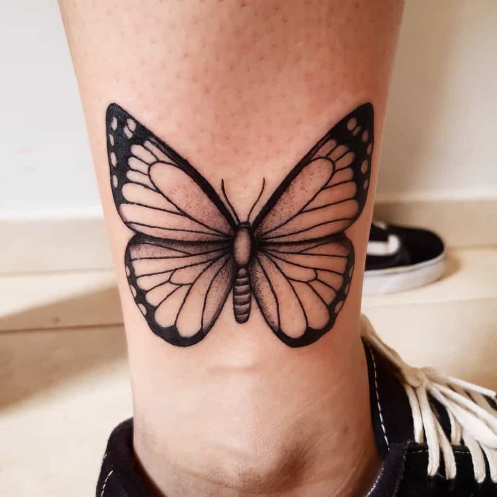 medium-sized black and grey tattoo on man's lower leg of realistic butterfly