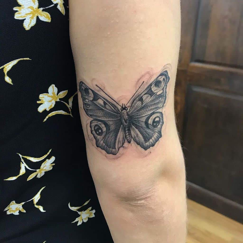 medium-sized black and grey tattoo on back of woman's upper arm of realistic butterfly