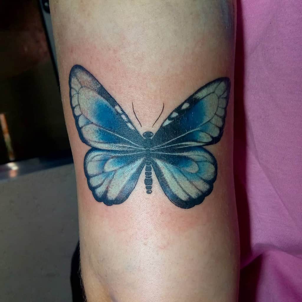 large color tattoo on woman's thigh of blue butterfly