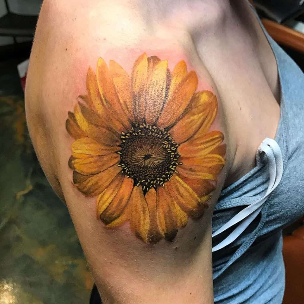 large color tattoo on woman's shoulder of realistic sunflower