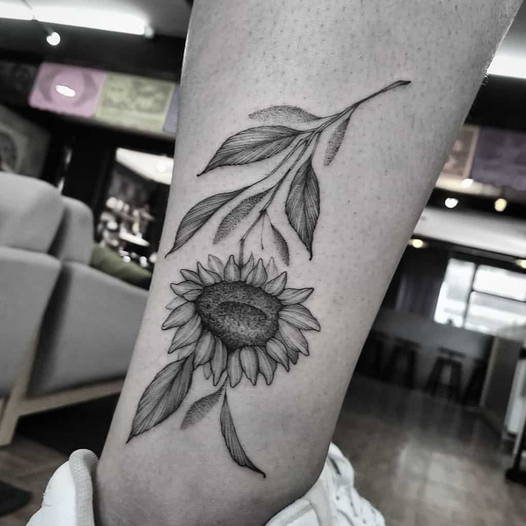 medium-sized black and grey tattoo on lower leg of upside down realistic sunflower with stem and leaves