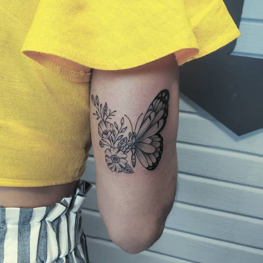 large black and grey tattoo on back of woman's upper arm of butterfly with one floral wing