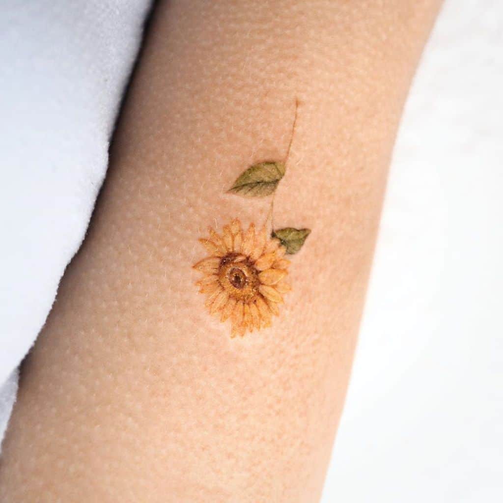 small color tattoo on woman of realistic sunflower with stem