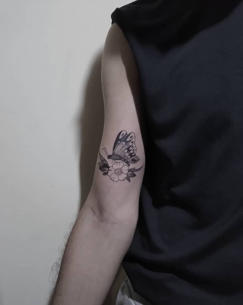 medium-sized black and grey tattoo on man's upper arm of realistic butterfly on a hibiscus flower