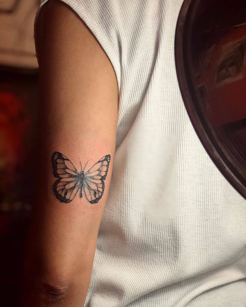 medium-sized black and grey tattoo on woman's upper arm of realistic butterfly