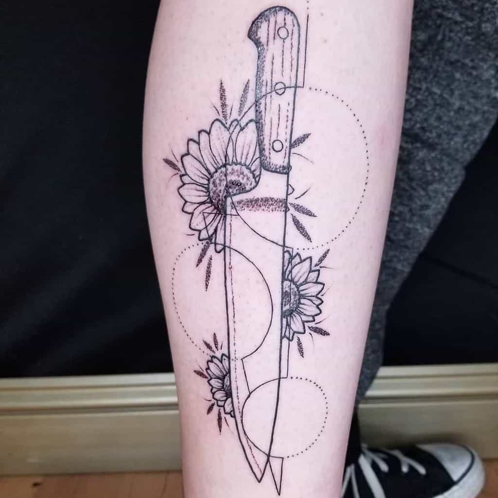 large black and grey geometric tattoo on woman's lower leg of knife with three sunflowers and circles behind it