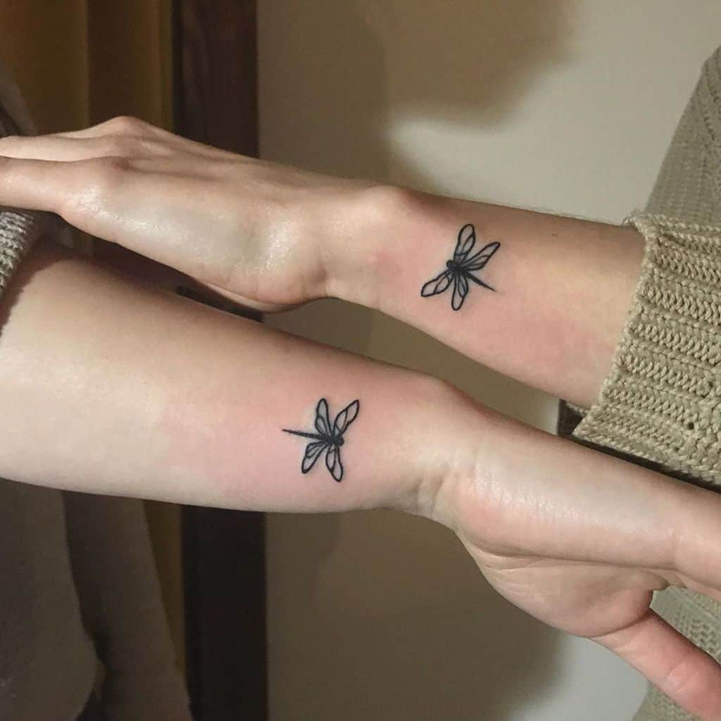 Two arms with identical dragonfly tattoos resonating the sense of friendship and harmony 