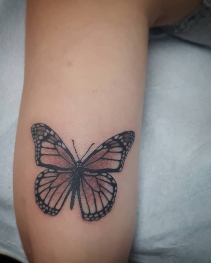medium-sized color tattoo on woman's upper arm of a realistic brown butterfly
