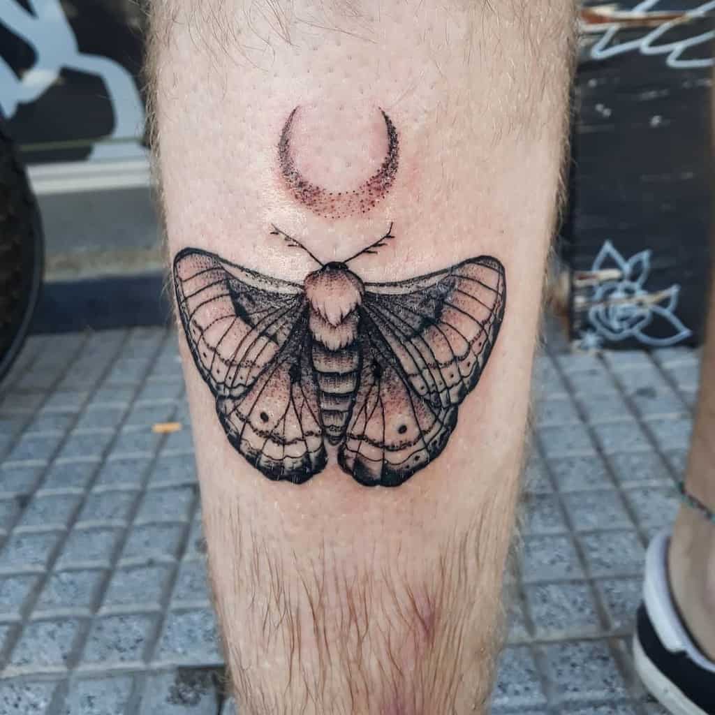 medium-sized black and grey tattoo on man's lower leg of a realistic detailed moth butterfly with crescent moon above