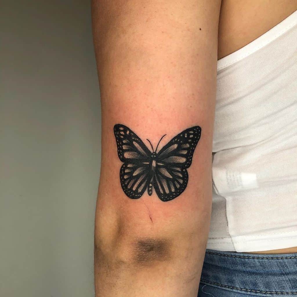 medium-sized black and grey tattoo on woman's upper arm of dark realistic butterfly
