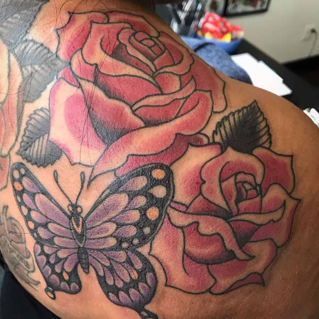 large color traditional tattoo on woman's upper back of a purple butterfly and three roses