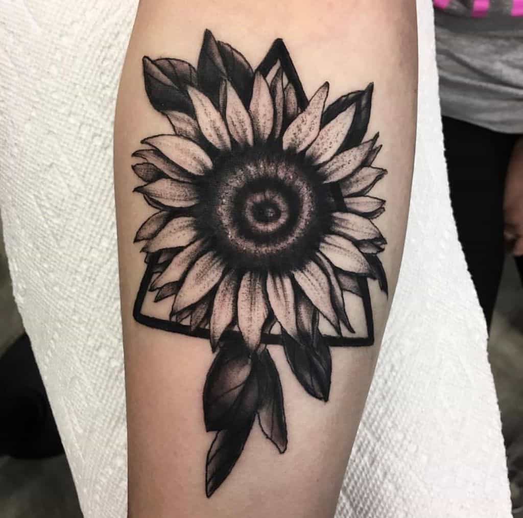 large black and grey bold tattoo on lower leg of realistic sunflower with geometric triangle and leaves around it