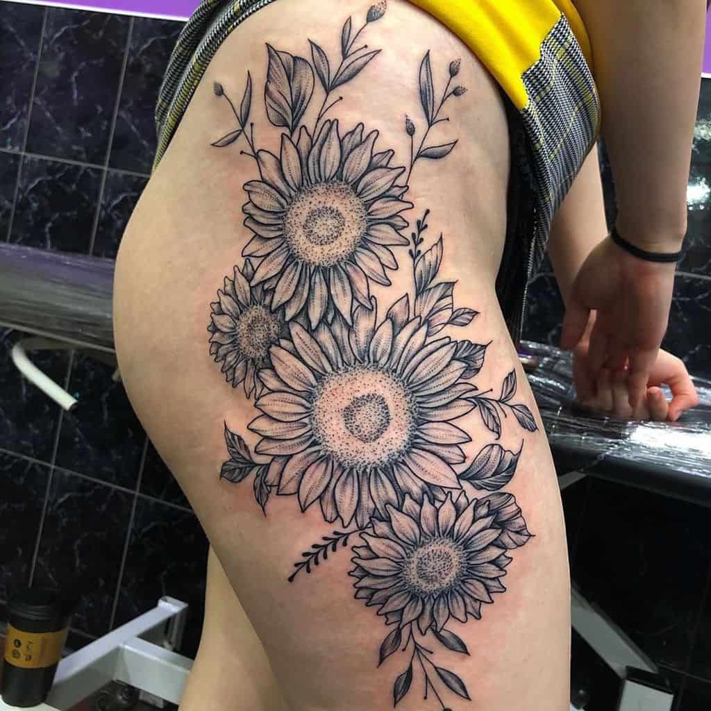 large black and grey realistic tattoo on woman's thigh of a bouquet of sunflowers