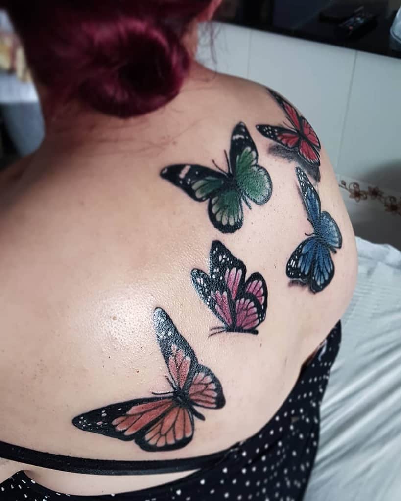 large color tattoos on a woman's upper back of multiple realistic butterflies