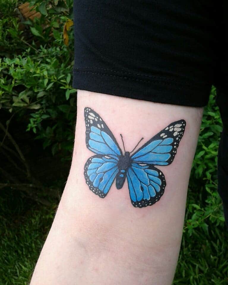 medium-sized color tattoo on upper arm of a realistic blue butterfly with white highlights