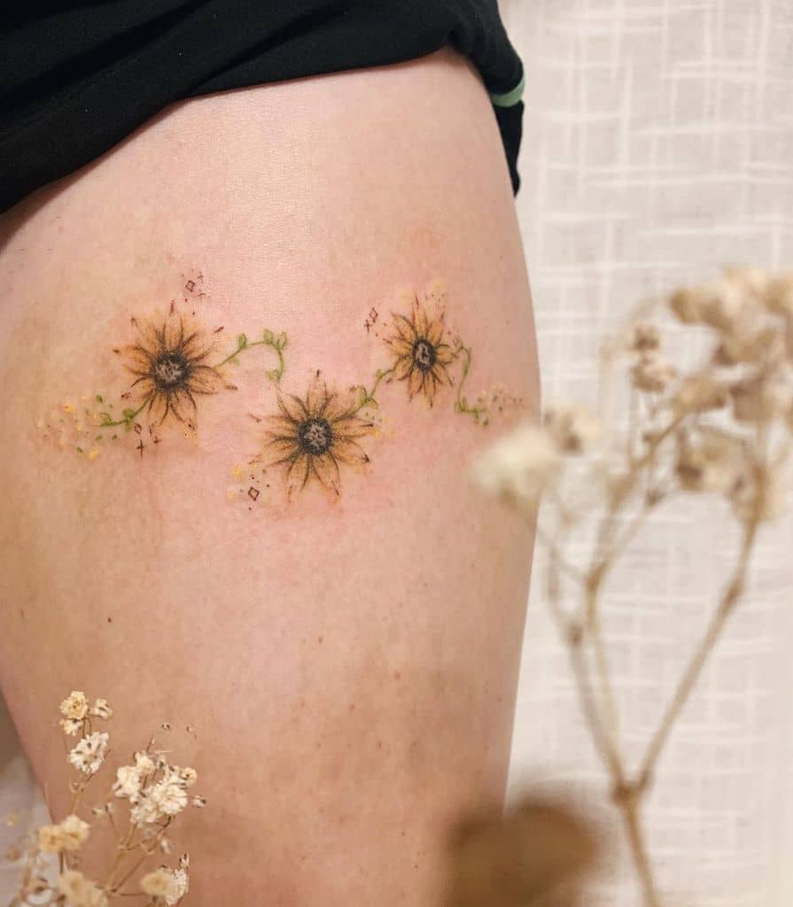 medium-sized tattoo on woman's thigh of three small colored sunflowers connected by vines