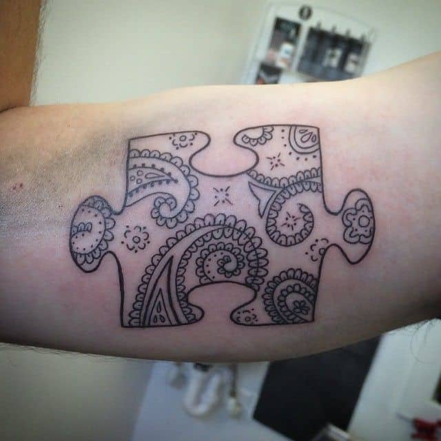 Black and gray bicep tattoo of a puzzle piece with paisley designs inside. 