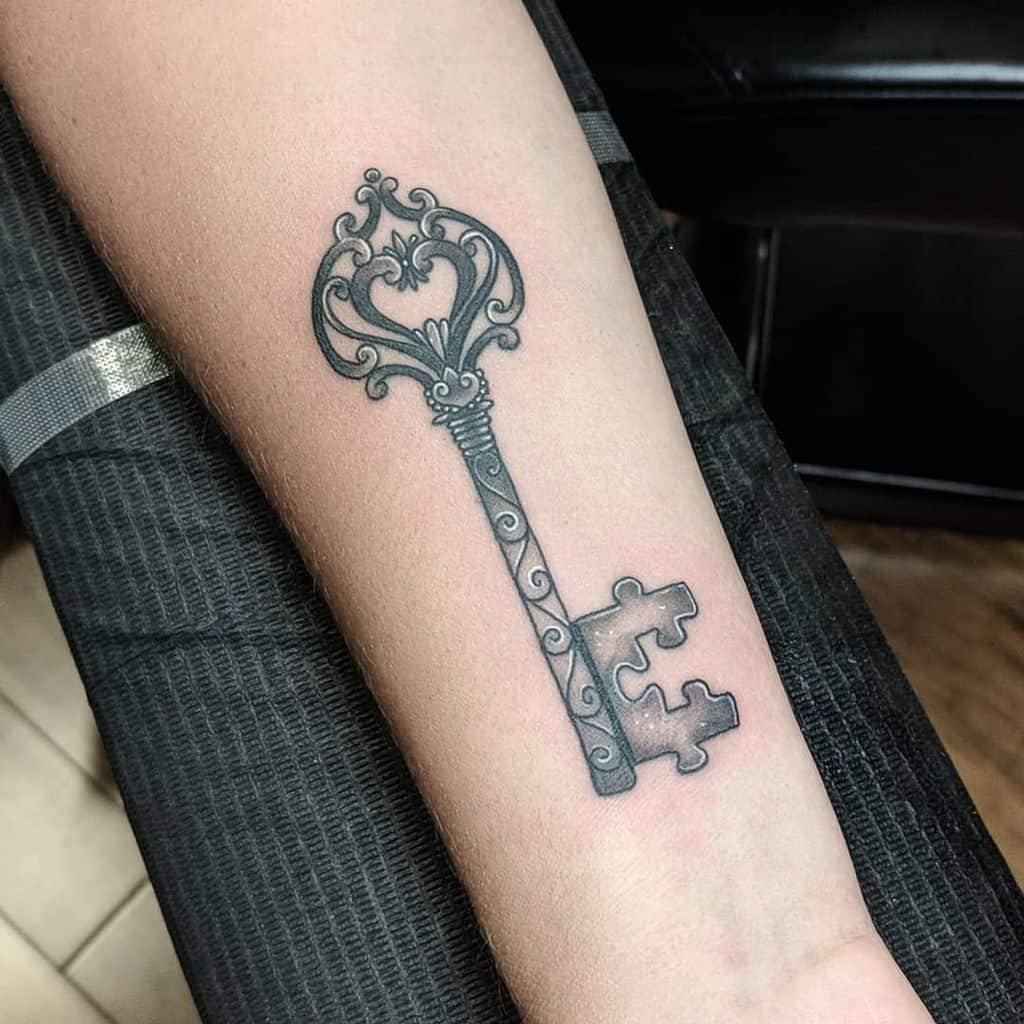 Black and gray forearm tattoo of an ornate skeleton key with puzzle piece for the bit.
