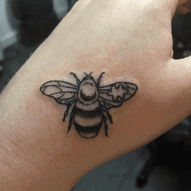 Black and gray hand tattoo of a bumble bee with a puzzle piece in its wing.