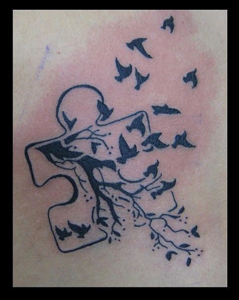 Black and gray tattoo of a puzzle piece with a tree and birds flying.