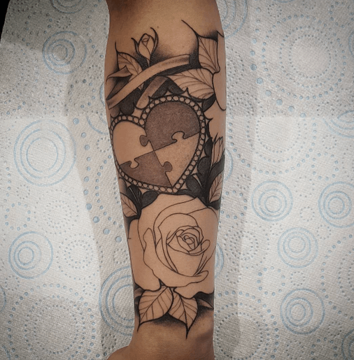 Black and gray unfinished forearm of puzzle piece heart and classic roses.