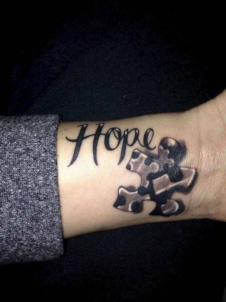 Black and gray wrist tattoo of “Hope” with a puzzle piece.