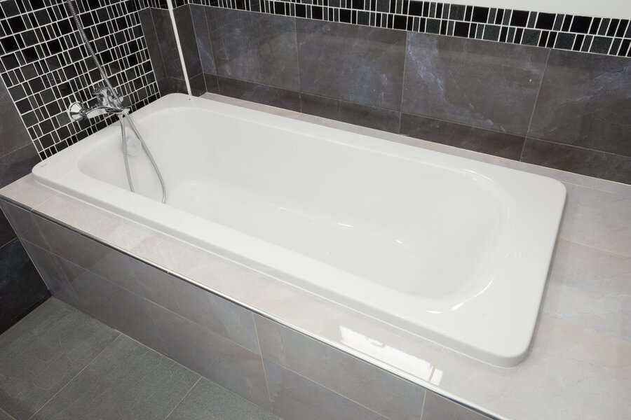 White built-in tub with handheld shower, surrounded by gray tiles and a black-and-white mosaic accent wall for a modern bathroom design