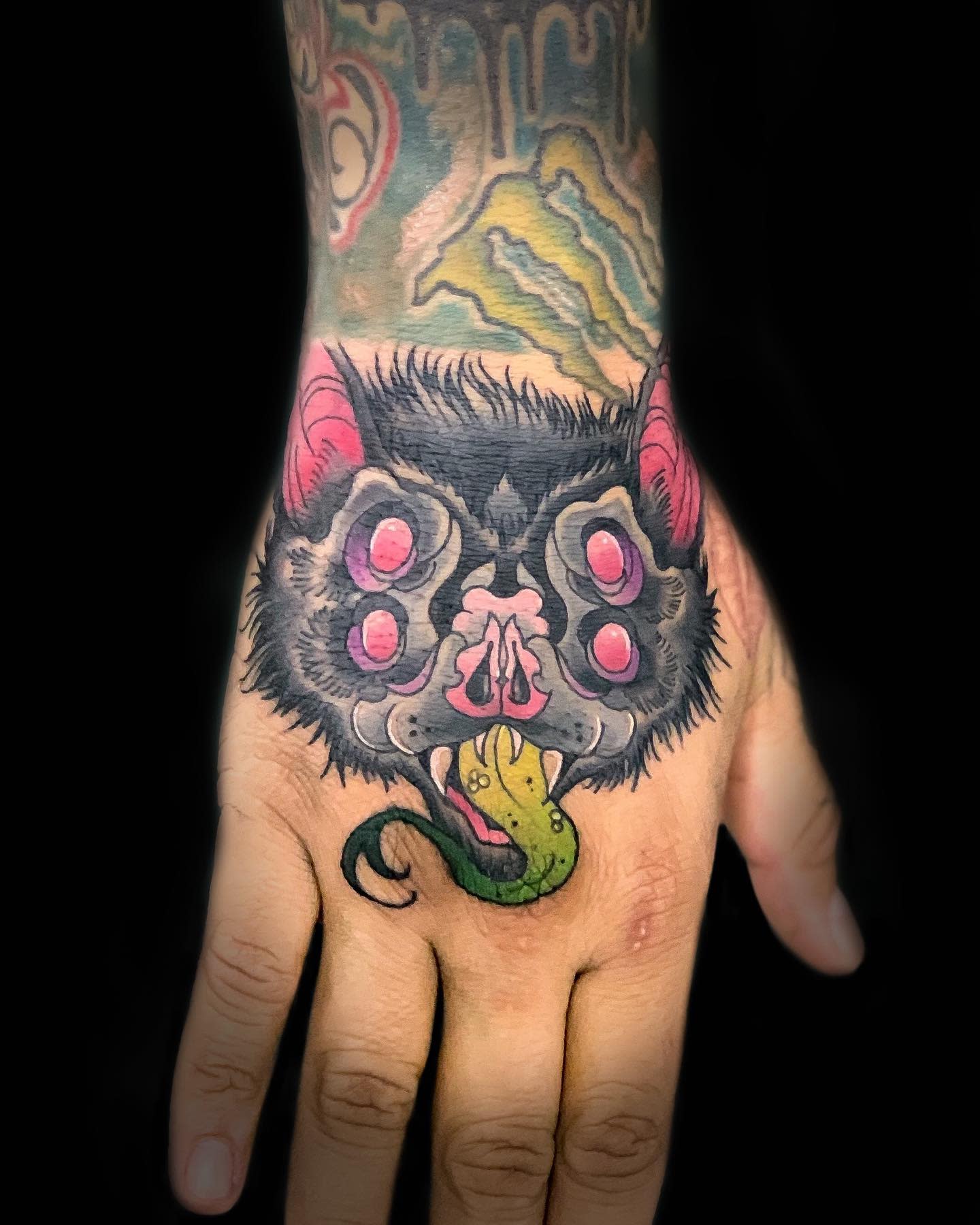 Colorful tattoo of a bat on a hand, with a green tongue emerging from its mouth