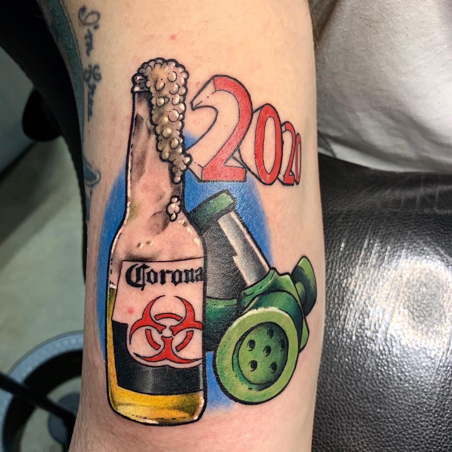 Tattoo of a beer bottle, biohazard symbol, gas mask, and "2020" text on an arm