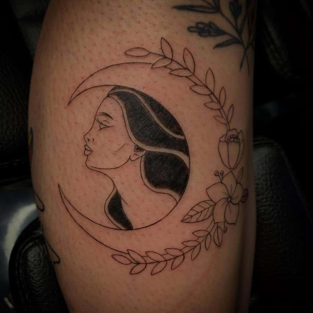 Tattoo of a woman's face in a crescent moon adorned with delicate flowers and leaves