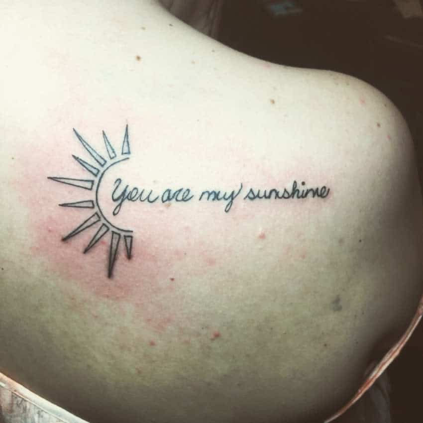 Tattoo of a sun design and the words "You are my sunshine" on the back of the neck