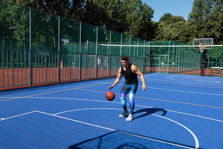 Person dribbling a basketball on an outdoor blue court, highlighting stylish and comfortable men's compression pants in bold colors