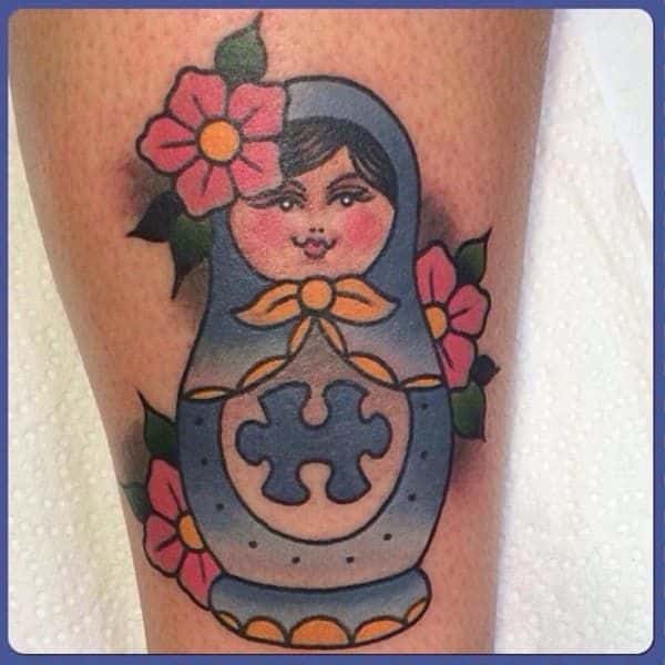 Full color calf tattoo of American traditional Russian nesting doll with flowers and a blue puzzle piece.