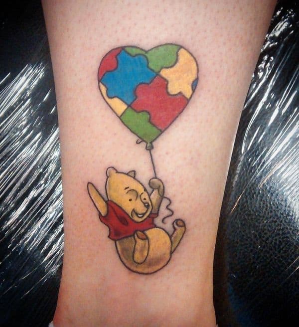 Full color calf tattoo of Winnie the Pooh falling with an Autism Awareness Puzzle heart balloon.