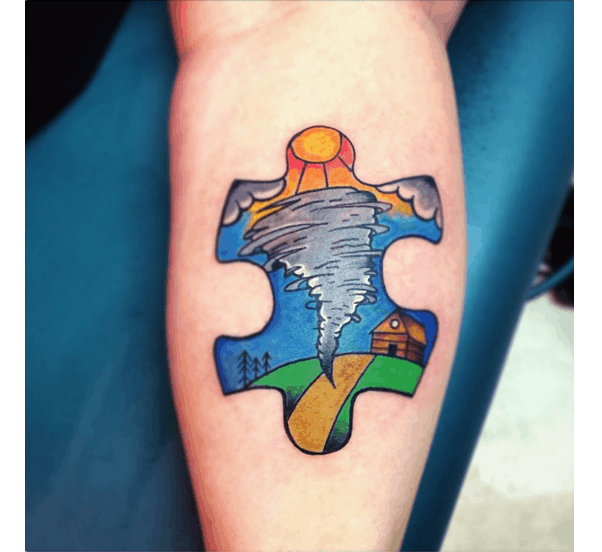 Full color calf tattoo of a puzzle piece with cartoon tornado, clouds and sun with trees and a barn.