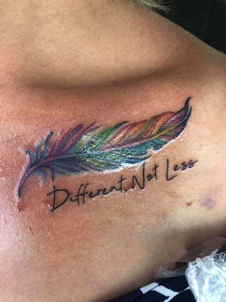 Full color collar bone tattoo of a multi-colored feather with script “Different Not Less”.