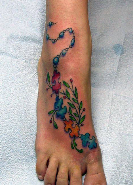 Full color foot tattoo of a chain of multi-colored puzzle pieces and beads with a tree branch. 