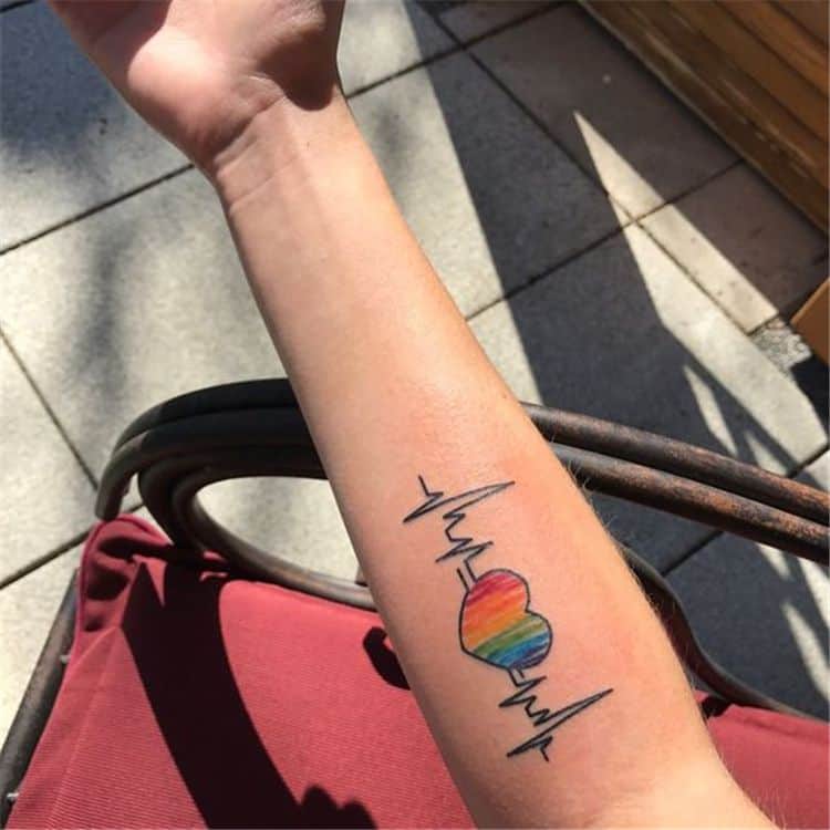 Full color forearm tattoo of a multi-colored heart with EKG readings on either side. 