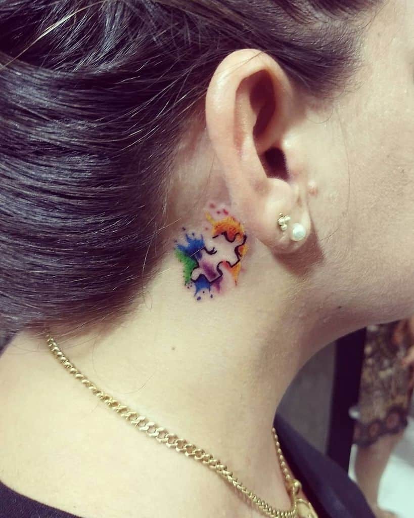 Full color puzzle piece tattoo behind the ear with watercolor splashes.