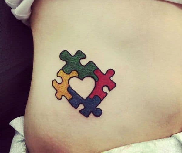 Full color rib tattoo of Autism Awareness Puzzle pieces with negative space heart.