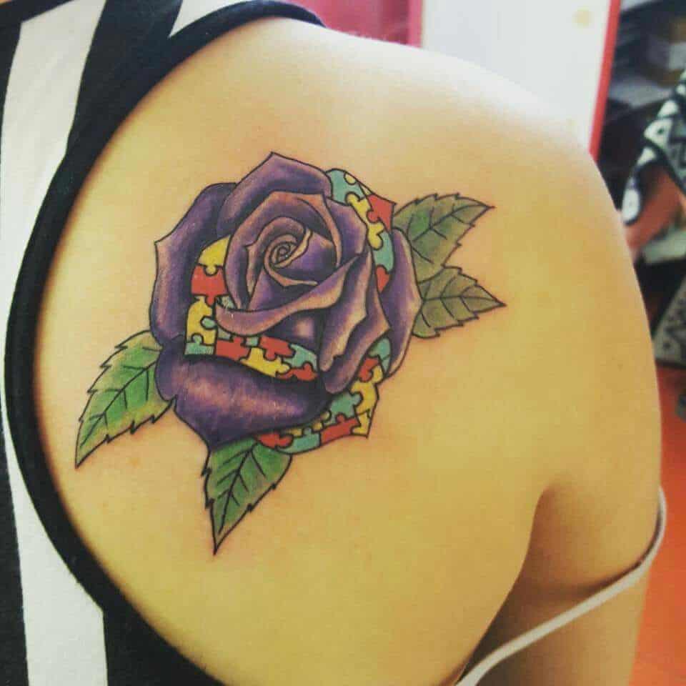 Full color shoulder blade tattoo of a purple rose with some Autism Awareness Puzzle petals.