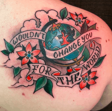 Full color shoulder blade tattoo with American traditional flowers and inspirational quote with globe missing a puzzle piece.