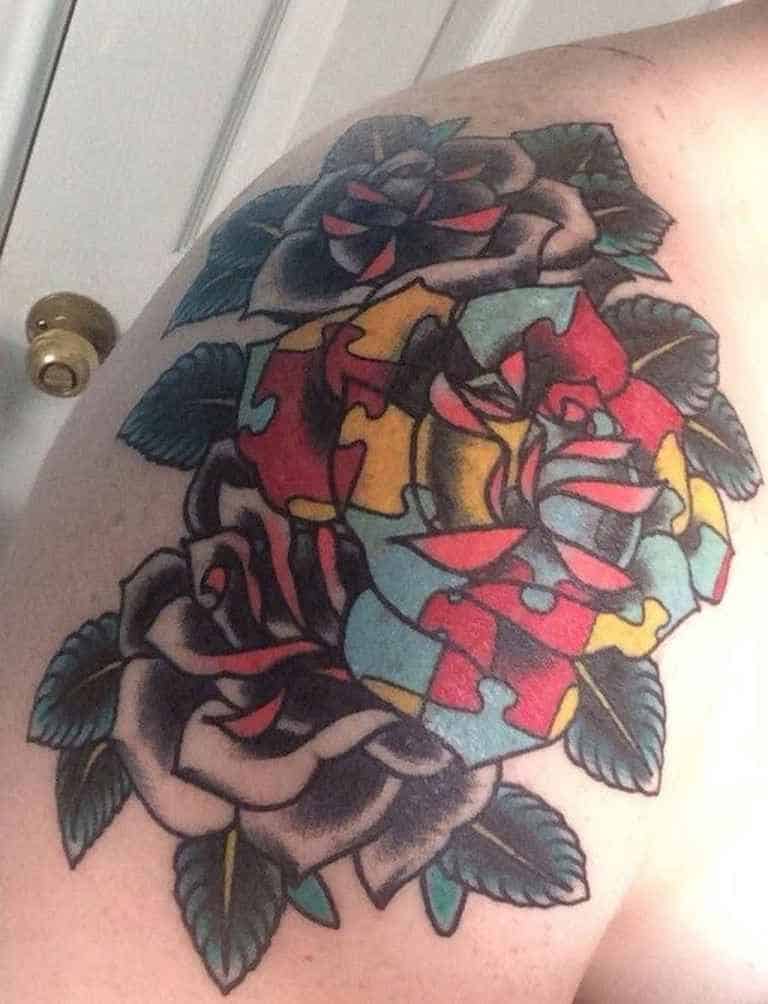 Full color shoulder tattoo of two black roses and one multi-colored puzzle piece rose. 
