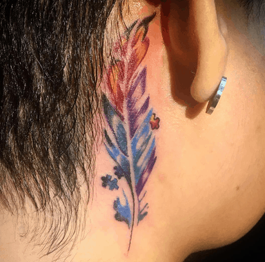 Full color tattoo behind the ear of a multi-colored, watercolor feather with puzzle pieces.
