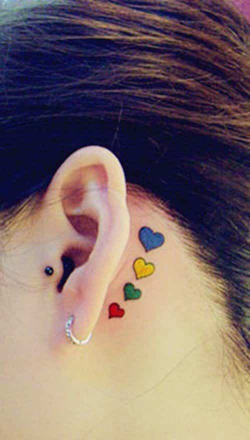 Full color tattoo behind the ear of four small hearts, red, green, blue and yellow.